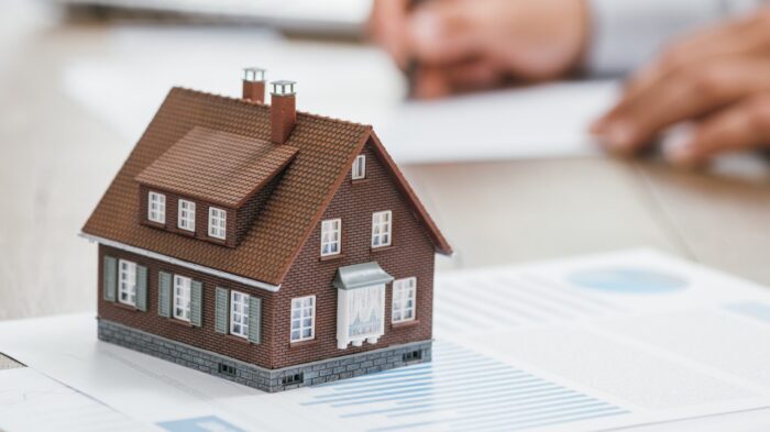 Real estate agent working in his office, he is writing a contract and house model on the foreground: investments, home loan and insurance concept